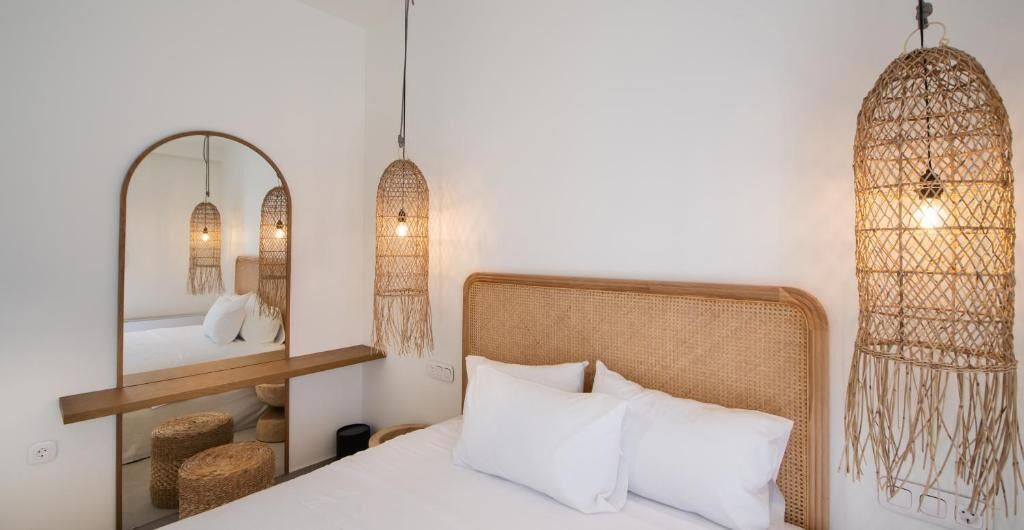 A bedroom with a large mirror, a bed with white bedding, and woven wall hangings.