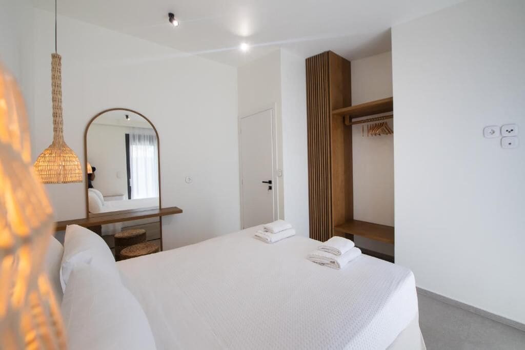A hotel room with a bed, a mirror, a hanging light fixture, a wardrobe, and a door.