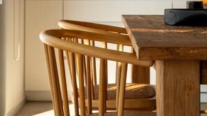 Una mesa de madera con sillas, una planta en maceta sobre una estantería y una encimera de cocina.