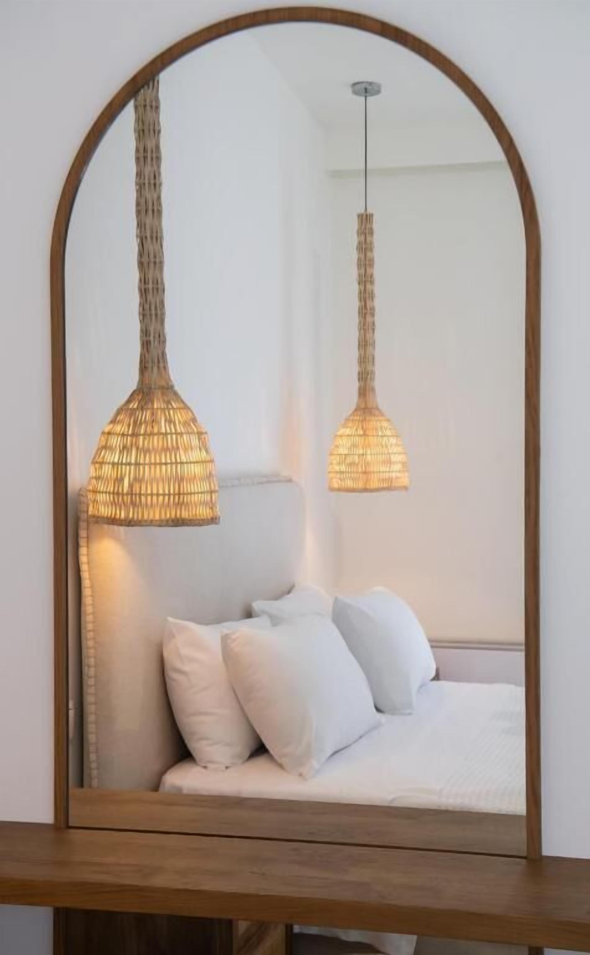 A bed with white bedding and two hanging lamps with a woven design.