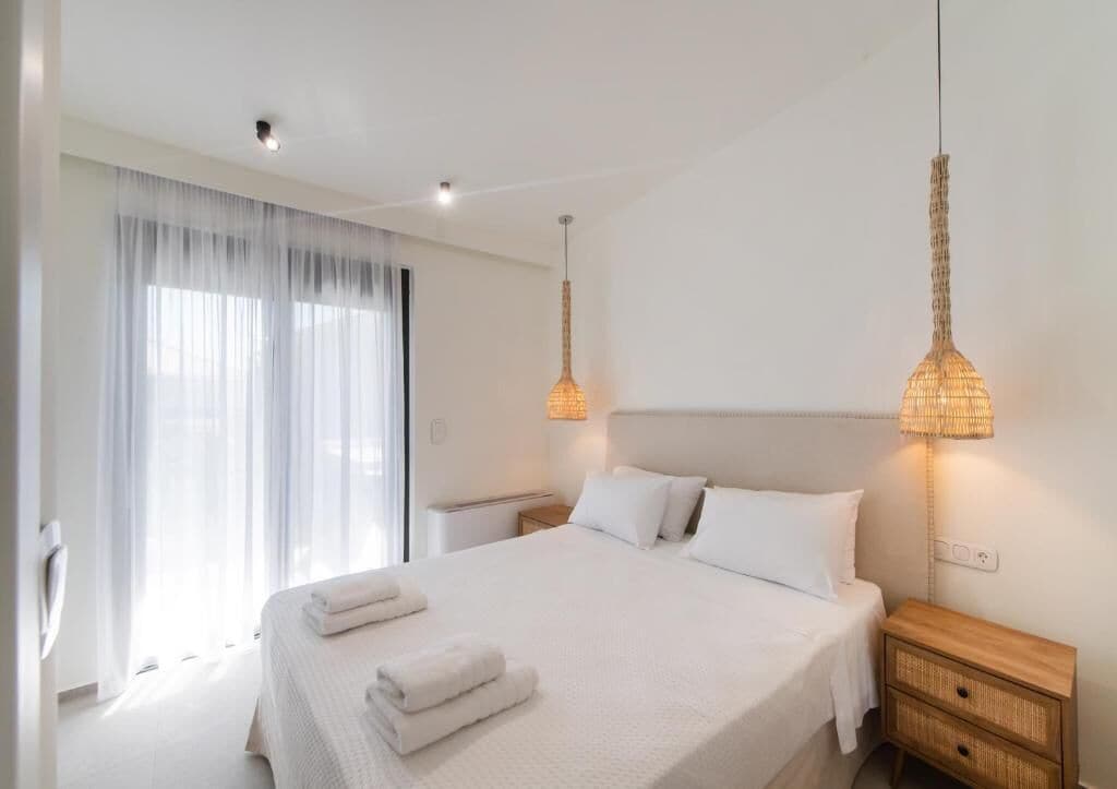 Ein Hotelzimmer mit einem großen Bett, Nachttischlampen, einem Nachttisch und einem Fenster mit transparenten Vorhängen.