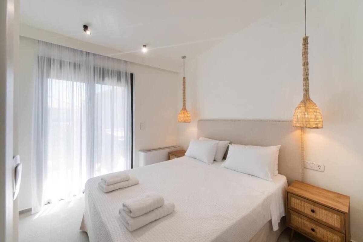 Une chambre d’hôtel avec un grand lit, des lampes de chevet, une table de nuit et une fenêtre avec des rideaux légers.