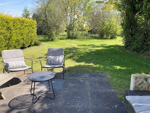 Eine Terrasse mit zwei Stühlen und einem kleinen Tisch, umgeben von einem grünen Garten und Bäumen.