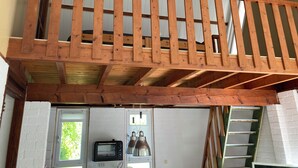 Una habitación estilo loft con balcón de madera, ventana con vistas, puerta y una pequeña cocina americana con microondas.