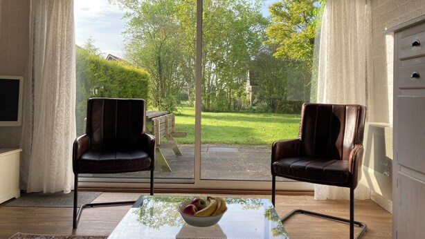 Una habitación con dos sillones de cuero, una mesa de vidrio con un frutero, y un cerramiento de vidrio corredera que da a un jardín.