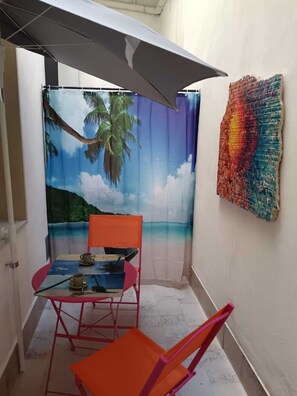 Ein kleiner Innenhof mit Tisch und Stühlen, ein Wandgemälde mit Strandmotiv und ein farbenfrohes Kunstwerk an der Wand.