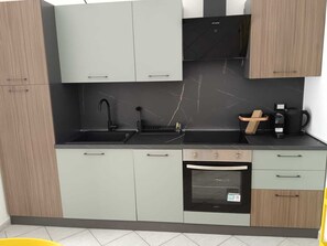 Eine moderne Küche mit grauen Schränken, einer schwarzen Arbeitsplatte, einer Spüle, einer Kaffeemaschine und einem Backofen.