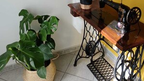 Et værelse med en vintage symaskine, en potteplante, et farverigt billede og en reol.
