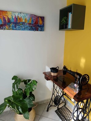 Ein Zimmer mit einer alten Nähmaschine, einem Blumentopf, einem farbenfrohen Gemälde und einem Bücherregal.