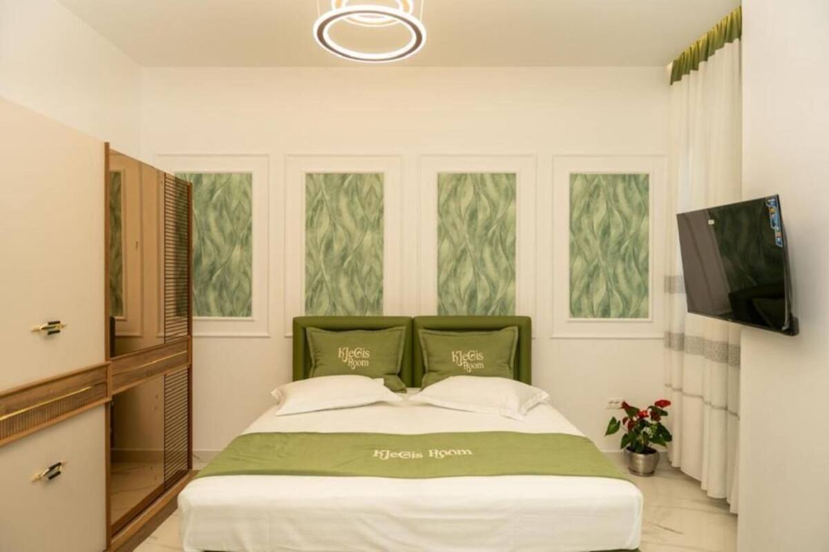 Habitación de hotel con cama, televisor, espejo y planta en maceta.