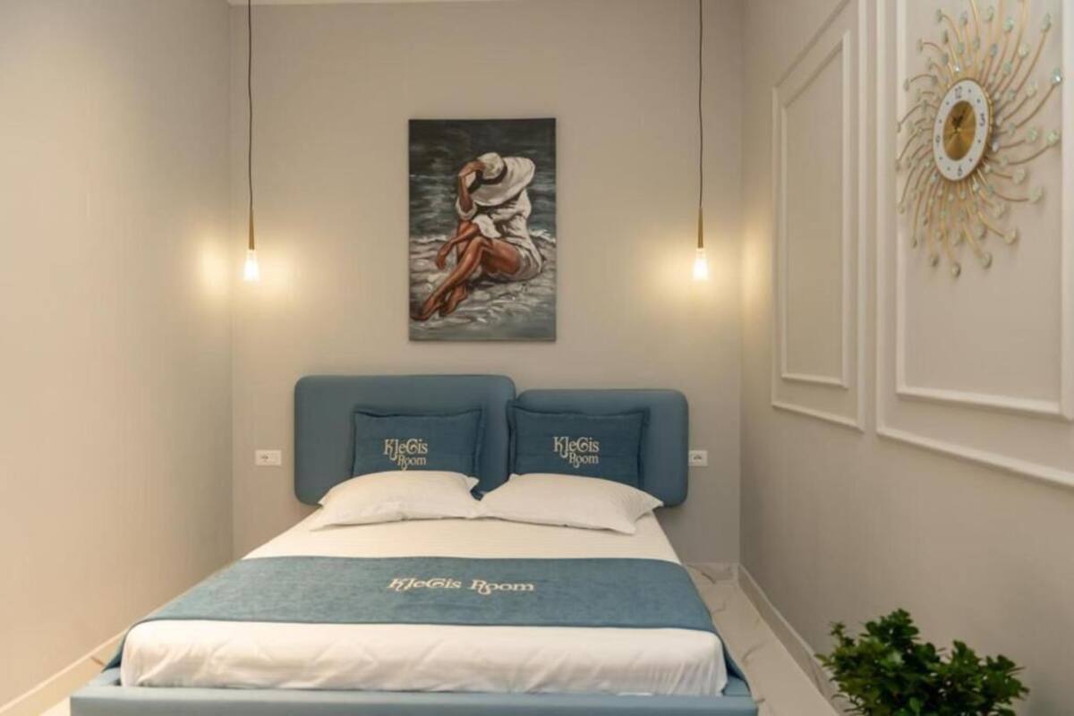 Un dormitorio con cama, dos almohadas, un reloj de pared y un cuadro.