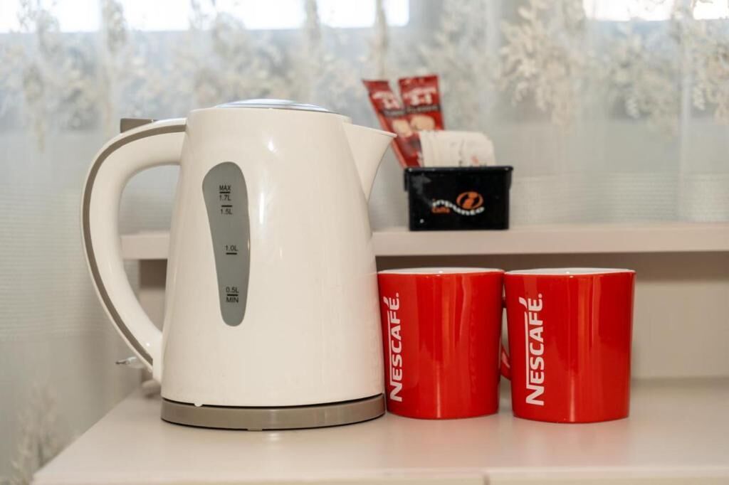 Una cafetera Nescafé blanca sobre una mesa, con dos tazas rojas de Nescafé a su lado.