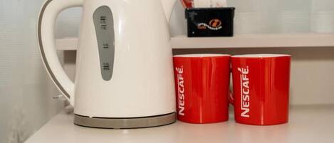 Una cafetera Nescafé blanca sobre una mesa, con dos tazas rojas de Nescafé a su lado.