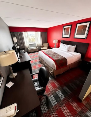 Habitación de hotel con cama, escritorio, silla y ventana con cortinas.