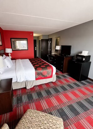 Une chambre d’hôtel équipée d’un lit, d’un bureau, d’une télévision, d’un four à micro-ondes et recouverte d’une moquette rouge.