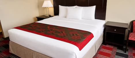 A hotel room with a large bed, a nightstand with a lamp, a chair, and a framed picture on the wall.