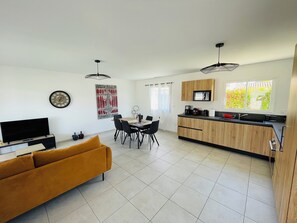 A modern kitchen with a dining area, a sofa, and a TV.