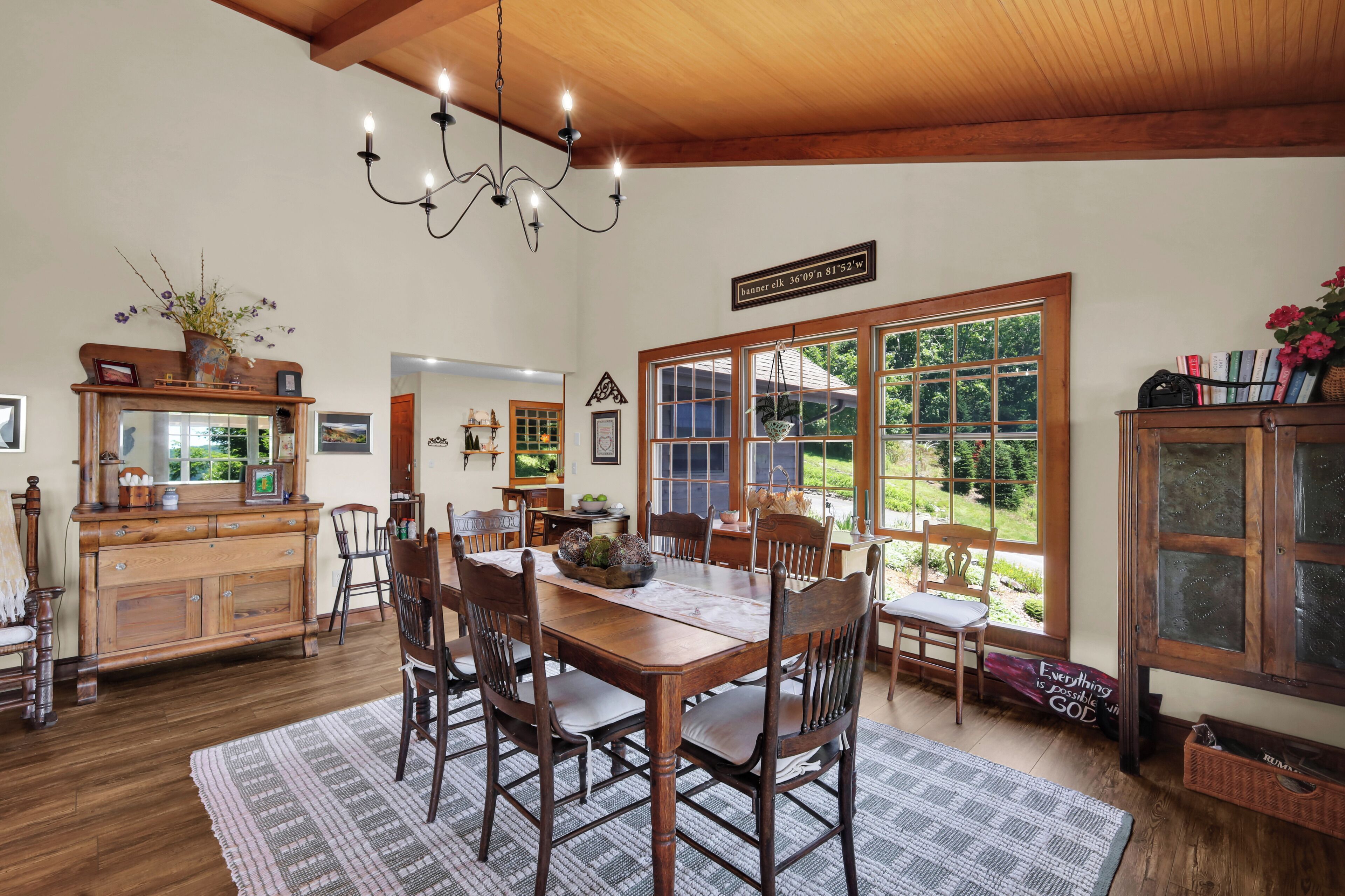 A dining area with a wooden table, chairs, a chandelier, and a view of the outdoors.