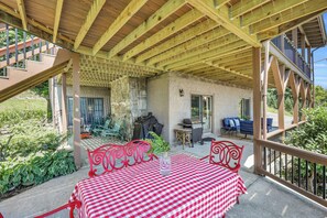 Ein überdachter Patio-Bereich mit einem karierten Tisch, roten Metallstühlen und einem Grill.