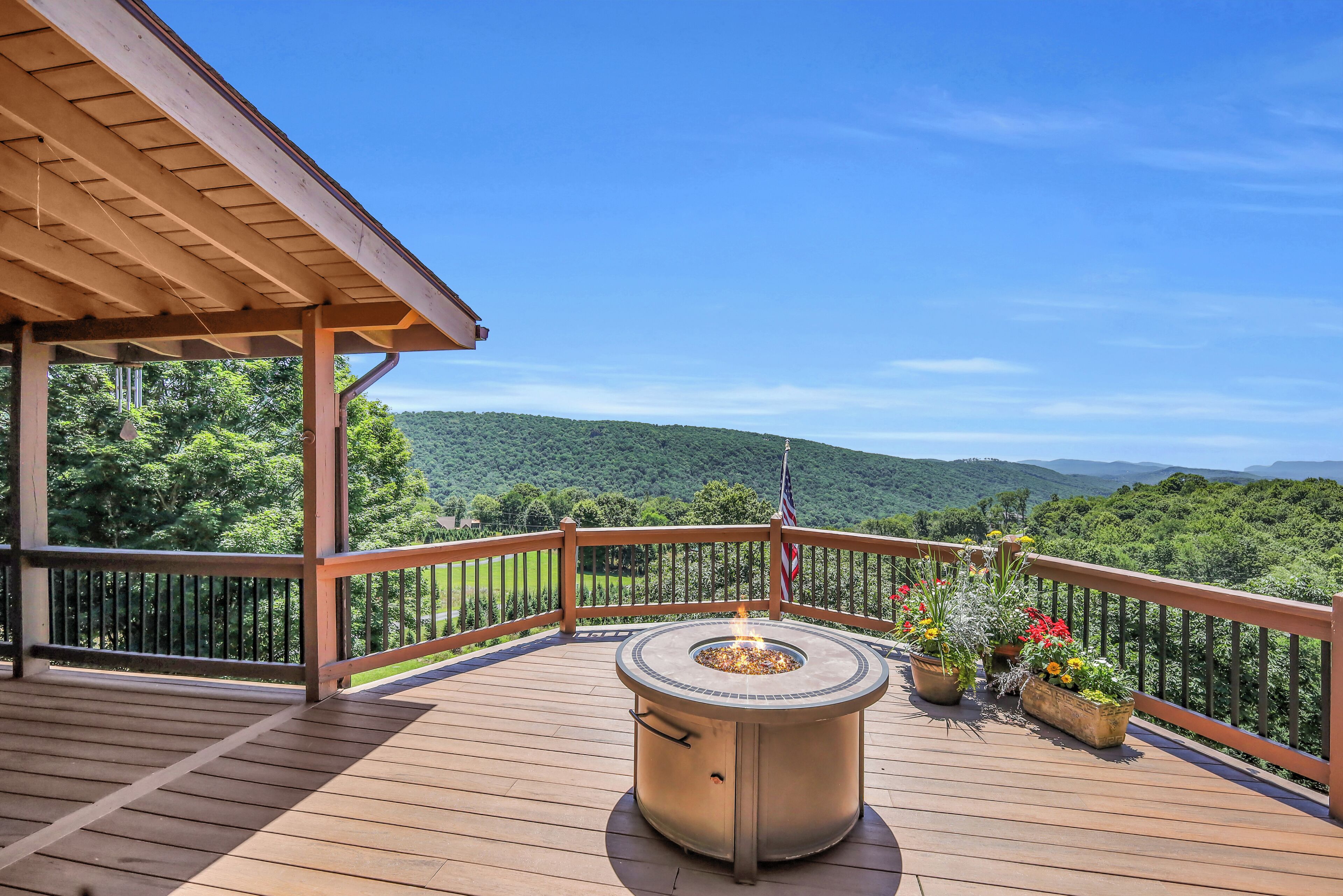 A wooden deck with a fire pit, potted plants, and a view of a forested mountain range.