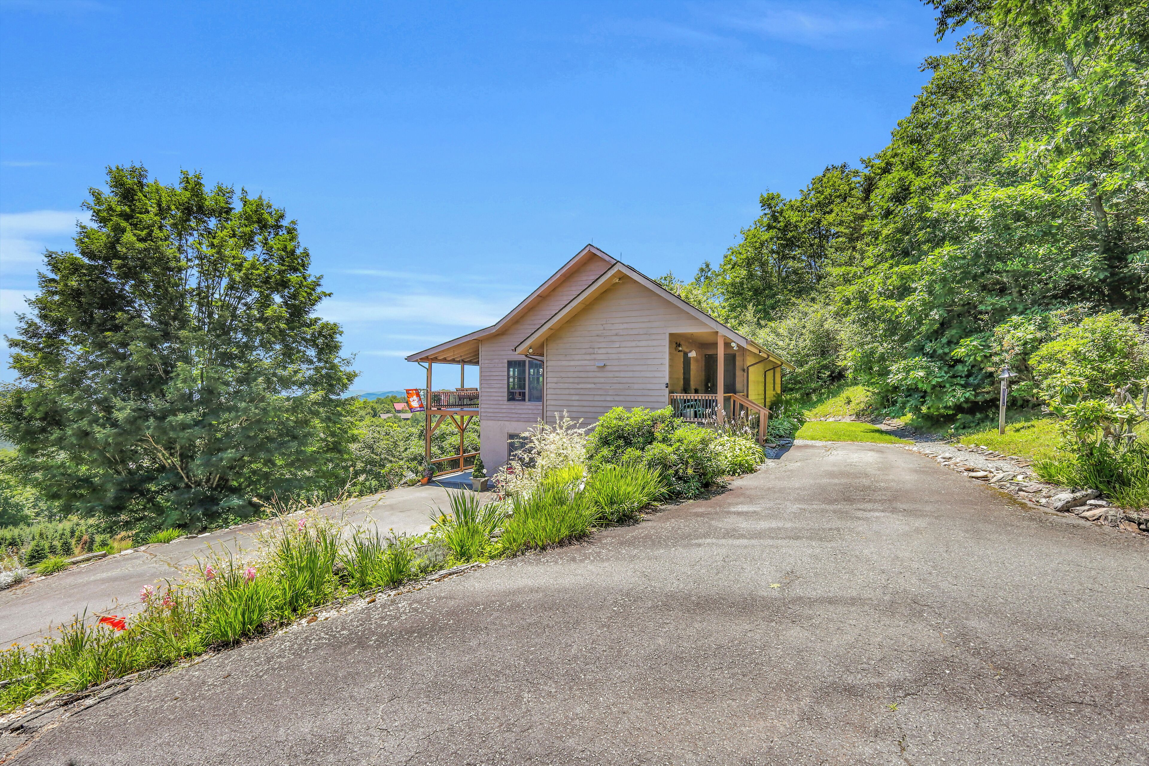 A single-story wooden cabin with a porch, surrounded by lush greenery and a clear sky.