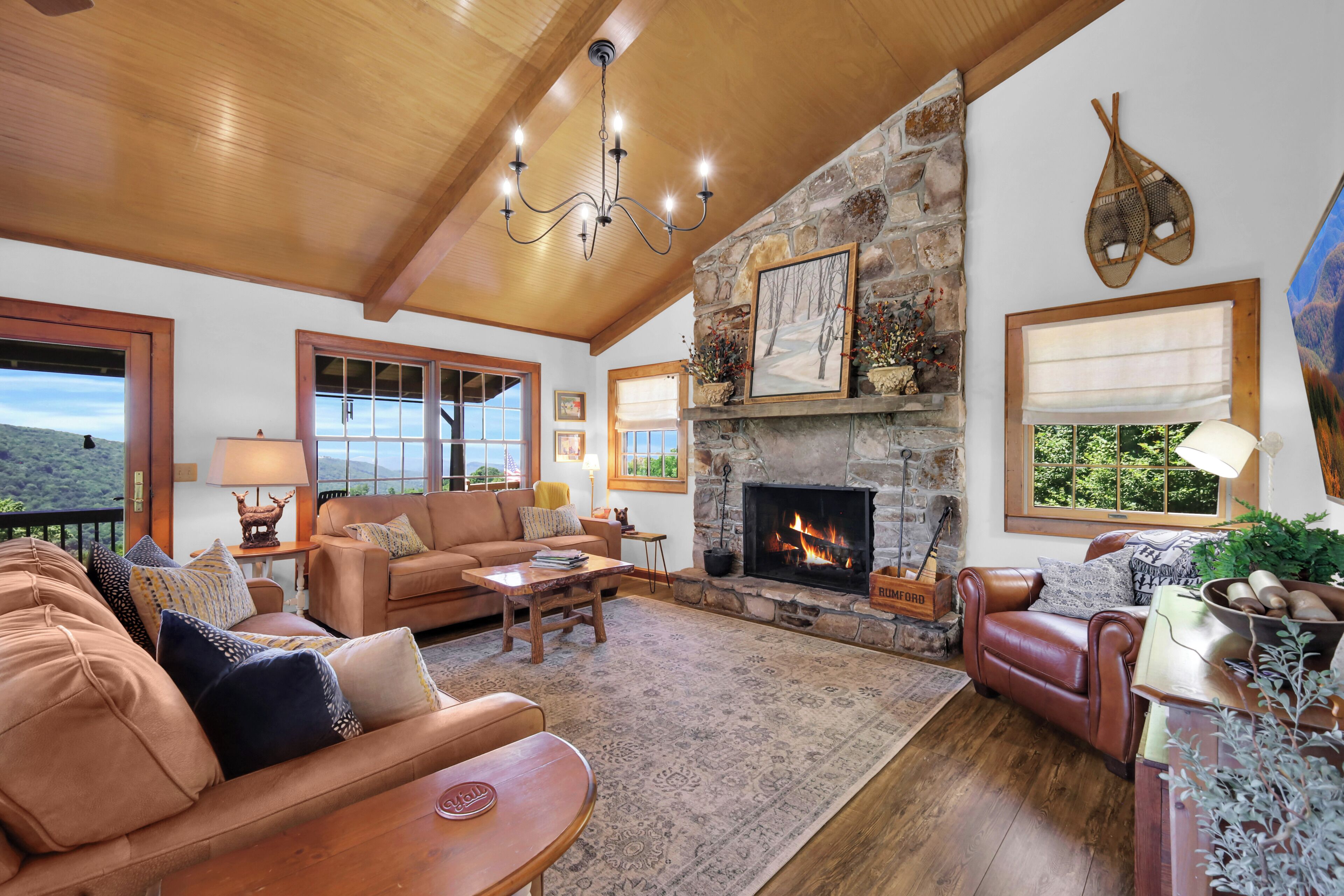 A spacious living room with a stone fireplace, leather sofas, and a large window overlooking a scenic landscape.