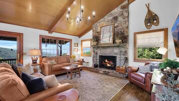 A spacious living room with a stone fireplace, leather sofas, and a large window overlooking a scenic landscape.