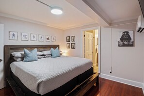 A bedroom with a bed, a wooden headboard, a bedside table, a wall-mounted air conditioner, and framed pictures on the wall.