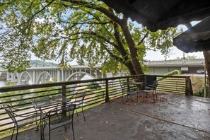 A covered outdoor seating area with metal chairs and tables, overlooking a bridge and greenery.