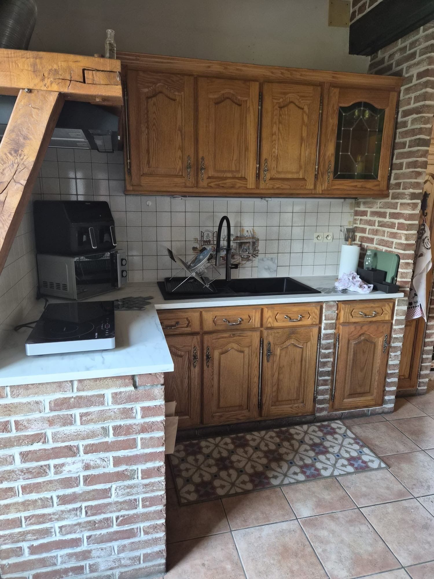 Une cuisine avec des meubles de rangement en bois, un mur d’accent en briques, un four encastré et un évier.