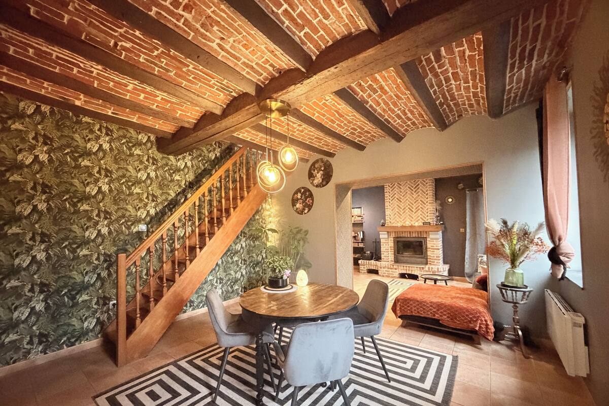 A cozy living room with a brick fireplace, a staircase, and a dining area with a patterned rug.