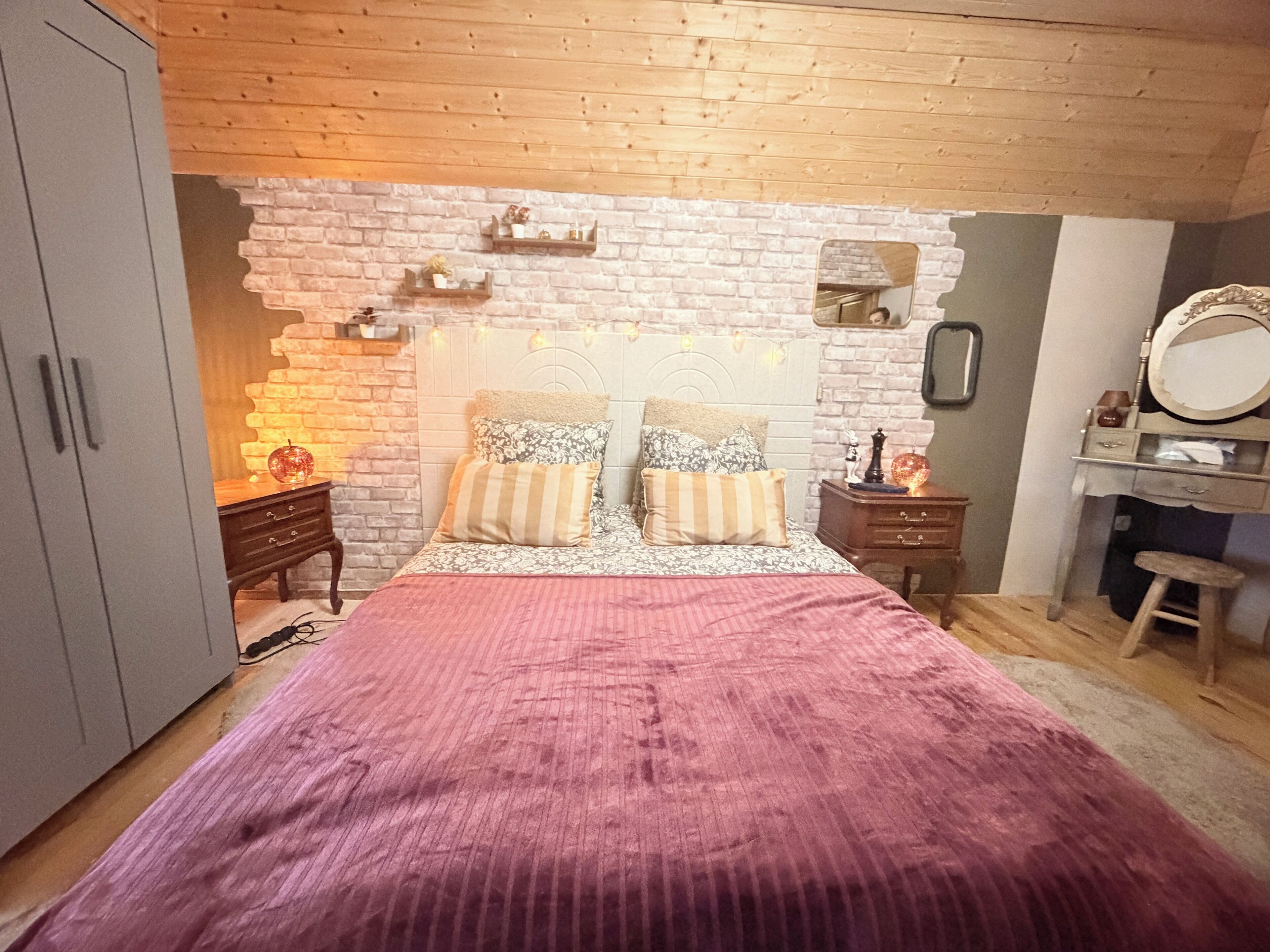 A bedroom with a bed, wooden headboard, a dresser, a mirror, and a wardrobe.