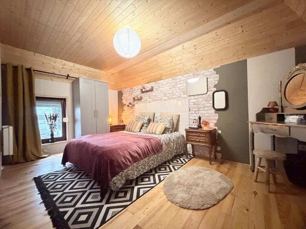 Une chambre avec un plafond en bois, un lit recouvert d’une couvre-lit à motifs, une table de chevet, une commode et un miroir.