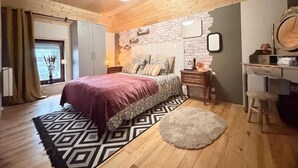 A bedroom with a wooden ceiling, a bed with a patterned bedspread, a nightstand, a dresser, and a mirror. - La clos de la ch'tite d'alsace (Crespin)