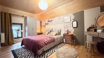 Une chambre avec un plafond en bois, un lit recouvert d’une couvre-lit à motifs, une table de chevet, une commode et un miroir.