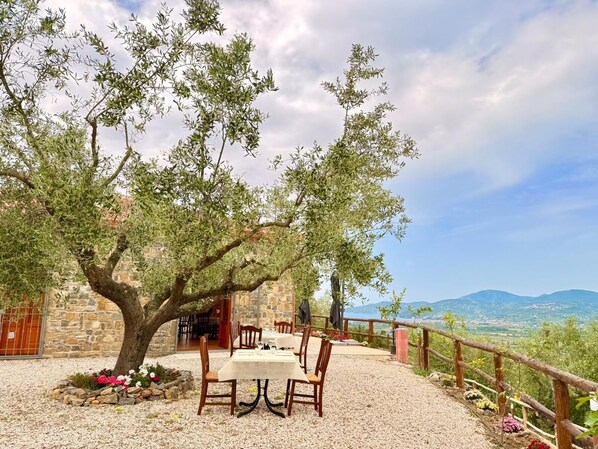 Un área de comedor al aire libre con mesa y sillas, un edificio de piedra y vistas al paisaje.