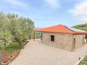 Un edificio de piedra con techo de tejas rojas, camino de grava y sendero bordeado de árboles.