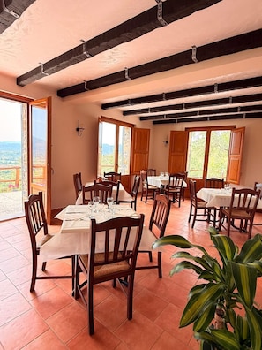 A dining area with tables and chairs, large windows, and a view of the outdoors.