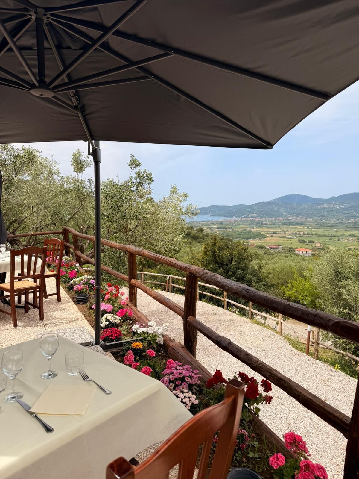 Ein Essbereich im Freien mit einem Tisch für zwei Personen, umgeben von einem Holzbalkon und Blick auf eine ländliche Landschaft.