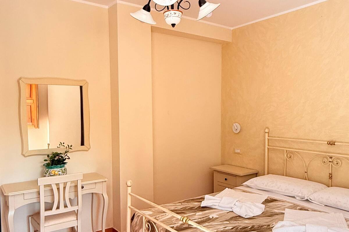 Una camera da letto con un letto, una scrivania, una sedia, uno specchio e una lampada a soffitto.