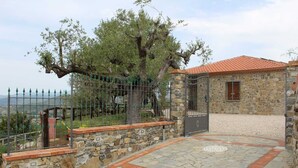 A stone building with a tiled roof, a metal gate, and a stone wall with a paved entrance. - Agriturismo il Carrubo (Ascea)