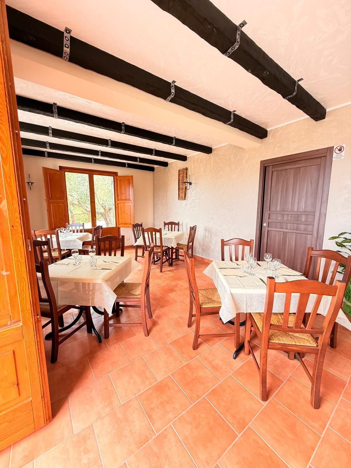 A dining area with wooden tables and chairs, a tiled floor, and a wooden door.