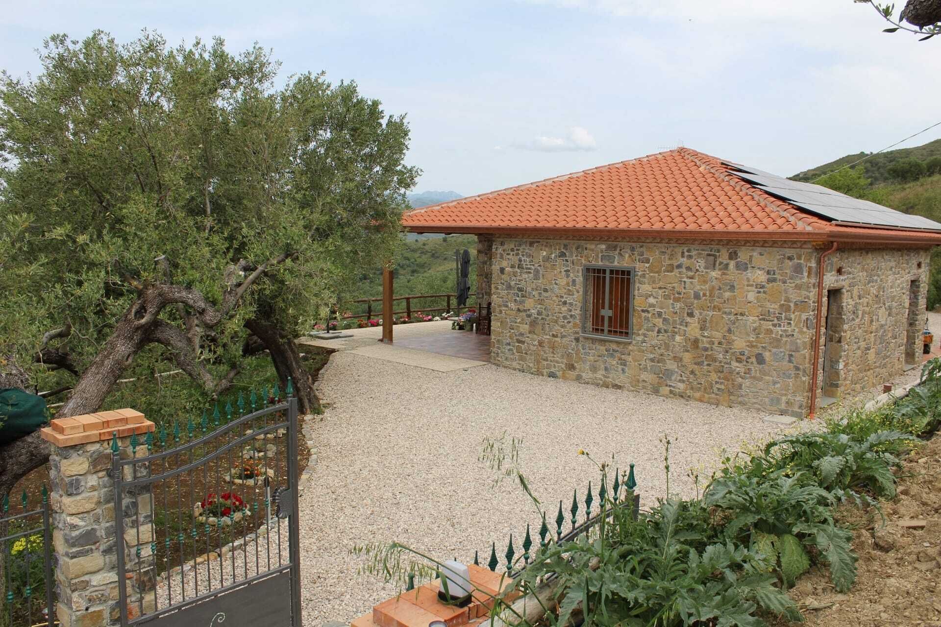 A stone building with a tiled roof, a gravel driveway, and a fenced garden area.