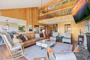 Ein großzügiger Wohnbereich mit hohen Decken, Holzwänden, einem Balkon, einem Kamin und einem Fernseher.
