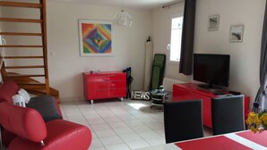 Uma sala de estar com um sofá vermelho, uma televisão, um armário vermelho, uma pequena mesa com um vaso e uma escada.