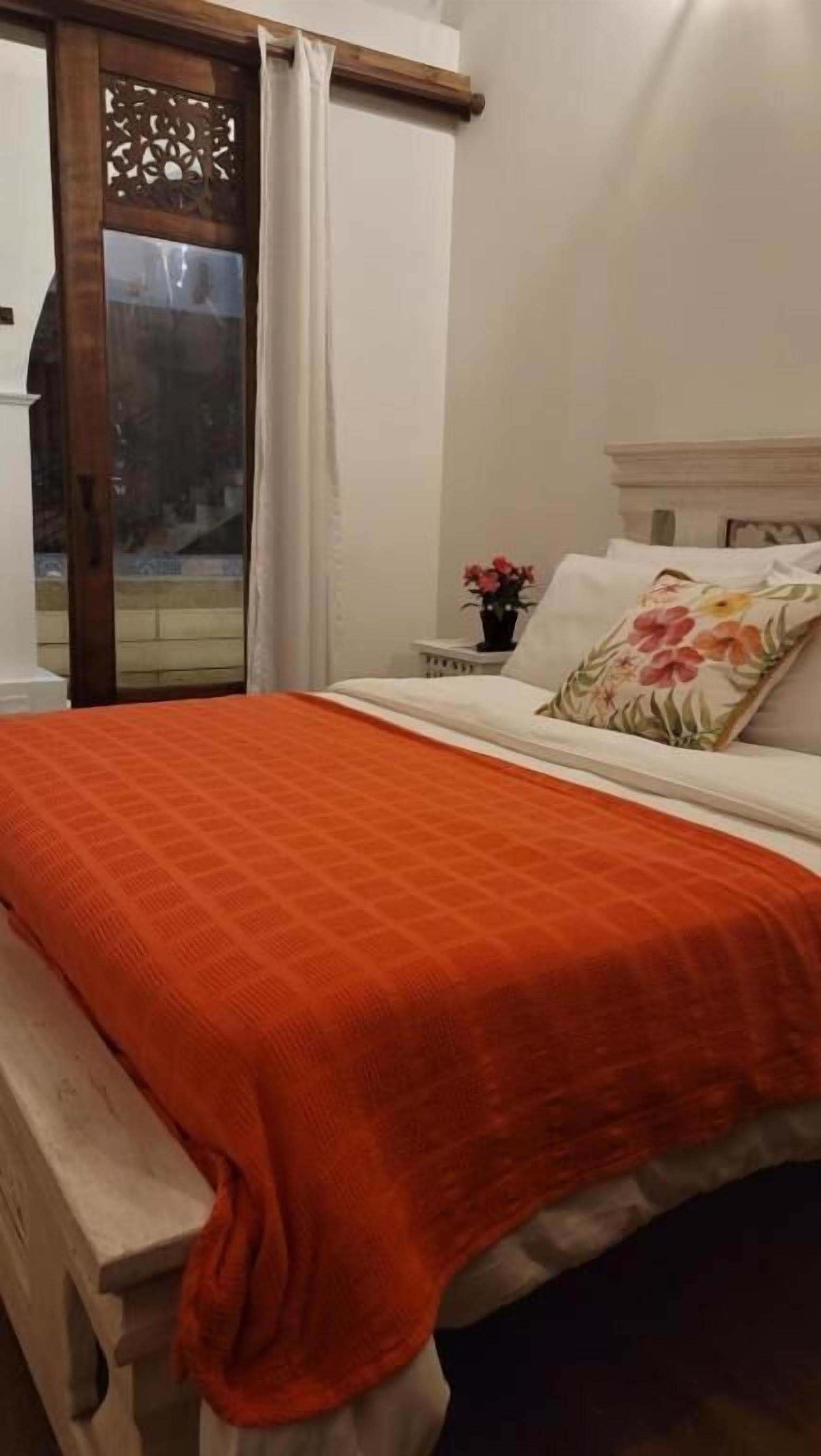 A bedroom with a bed, a nightstand, a window with curtains, and a view of the outside.