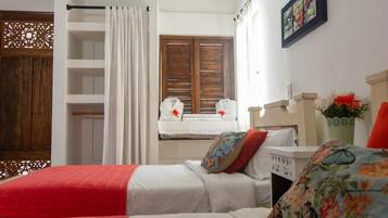 Un dormitorio con dos camas, una ventana con contraventanas de madera, una cortina blanca y un panel decorativo en la pared.
