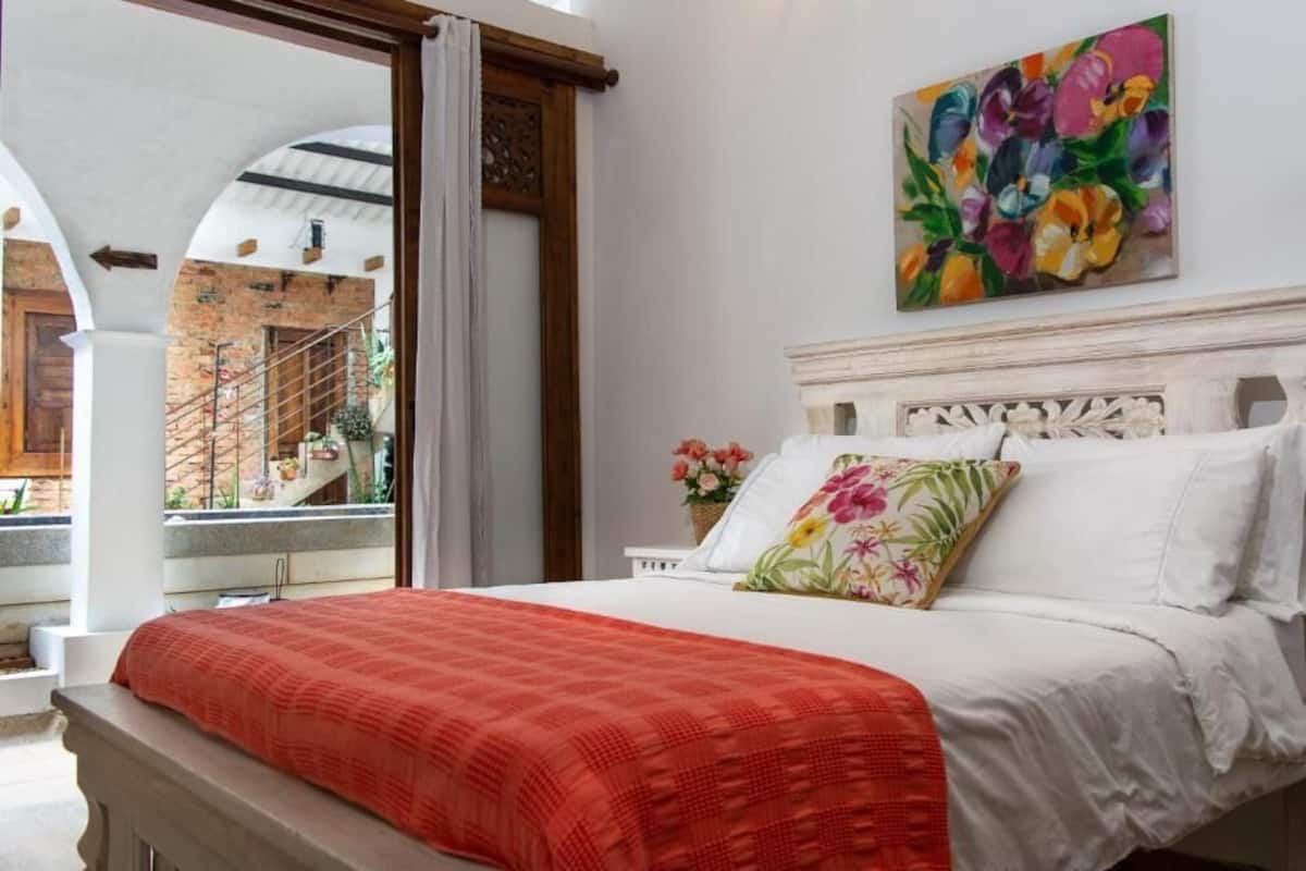 A bedroom with a bed, a painting, and a view of a staircase.