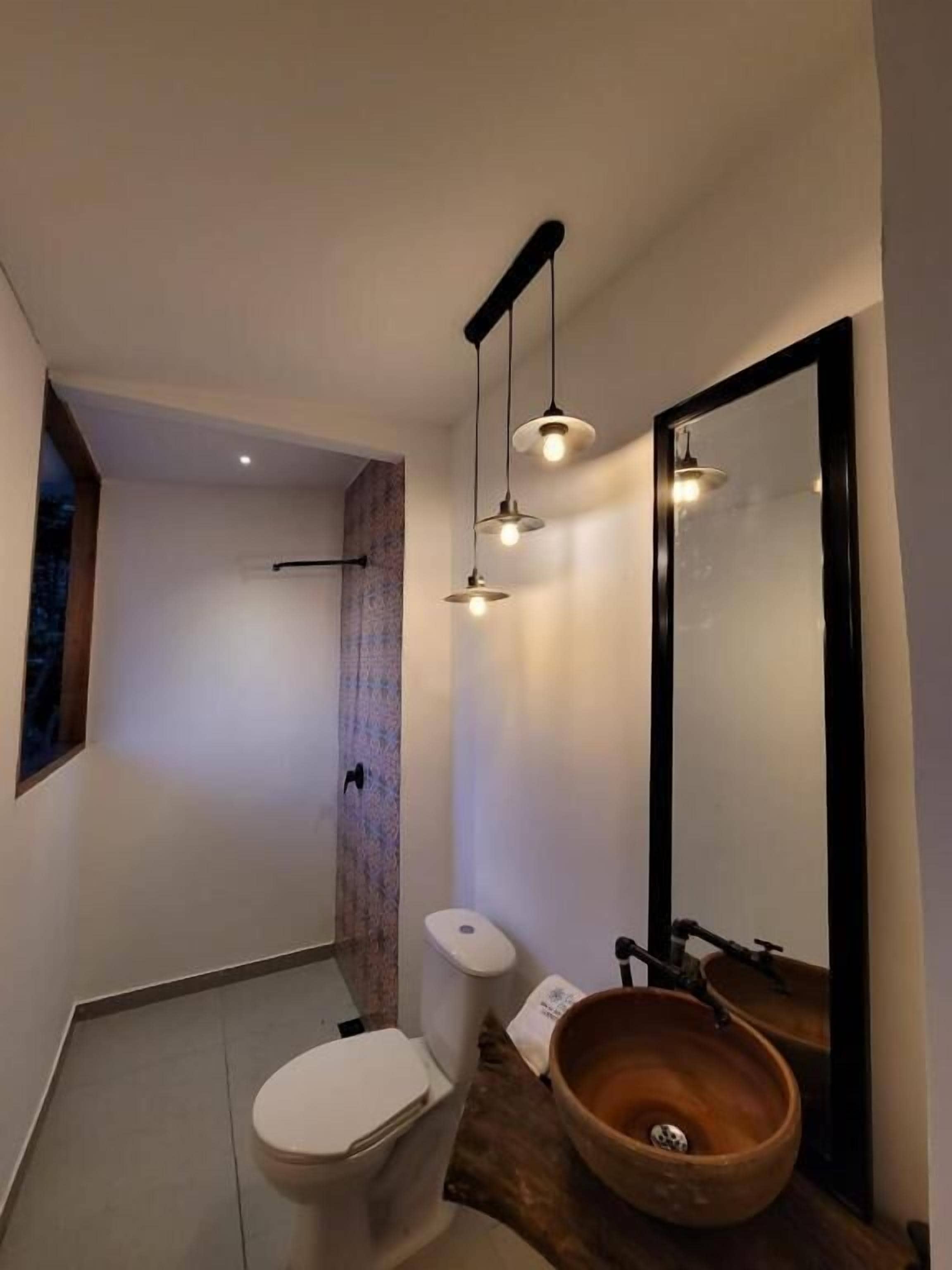 Une salle de bain moderne avec des toilettes blanches, un lavabo en forme de bol en bois et un éclairage suspendu.