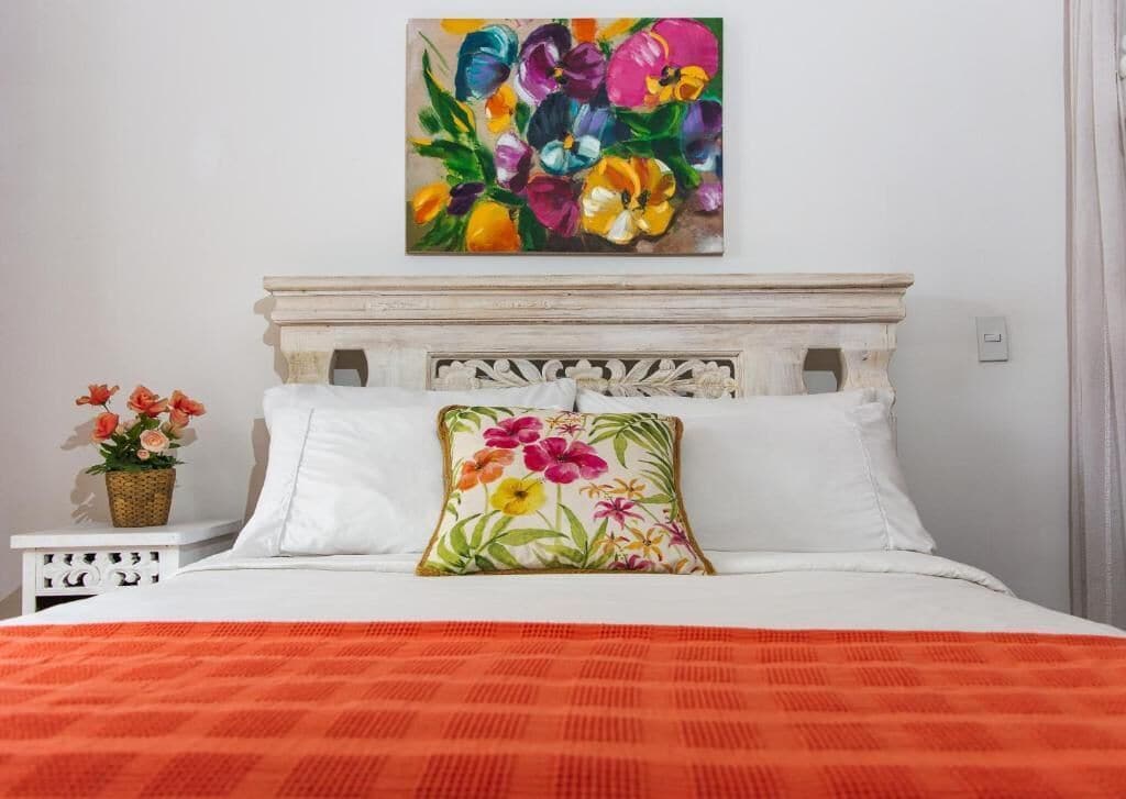 A bed with white bedding, a colorful floral pillow, and a painting above it.